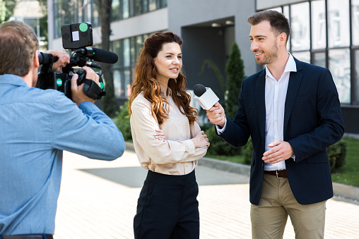 professional cameraman and male news reporter interviewing smiling businesswoman