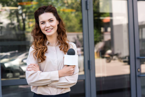 istock attractive female journalist holding microphone and looking at camera 1011129200