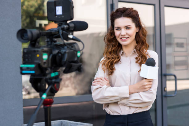 istock smiling journalist with microphone standing in front of digital video camera 1011129260