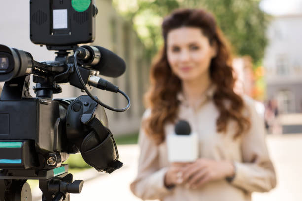 istock selective focus of journalist with microphone standing in front of digital video camera 1011129392