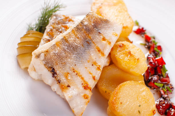 istock Roasted cod, codfish with baked potatoes and vegetables with pickled cucumber and herbs sauce on a white background Restaurant serving. restaurant menu 1011138460