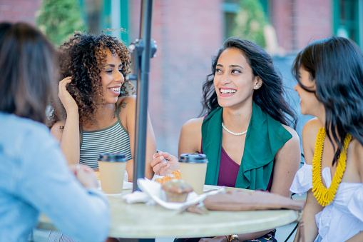 A group of young women are outdoors in an urban area. They are chatting and enjoying coffee.