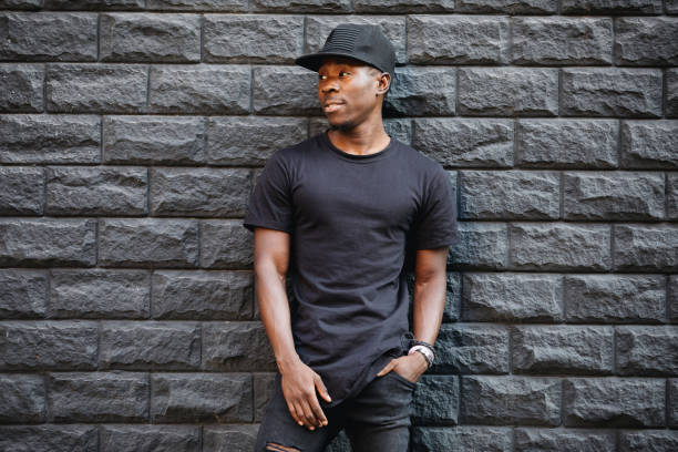 handsome african american man in blank black t-shirt standing against brick wall - black backgound imagens e fotografias de stock