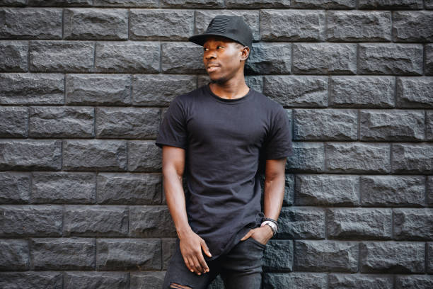 красивый афроамериканец в пустой черной футболке, стоящей у кирпичной стены - black cap стоковые фото и изображения