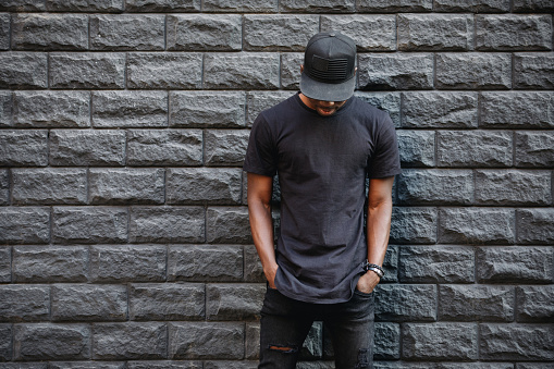 Guapo hombre afroamericano en blanco permanente de camiseta negra contra la pared de ladrillo photo