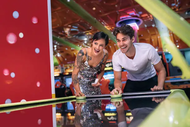 Couple holding strikers and playing air hockey game as a team at a gaming parlour. Man and woman having fun playing games at a gaming arcade.