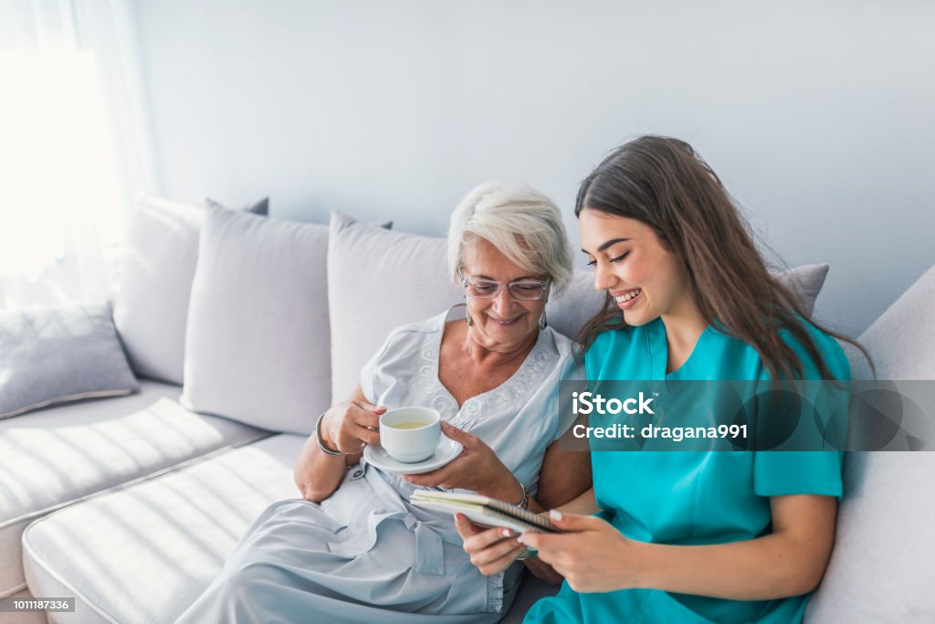 Aged elegant woman and tea time at nursing home Happy patient is holding caregiver for a hand while spending time together. Elderly woman in nursing home and nurse. Aged elegant woman and tea time at nursing home Senior Adult Stock Photo
