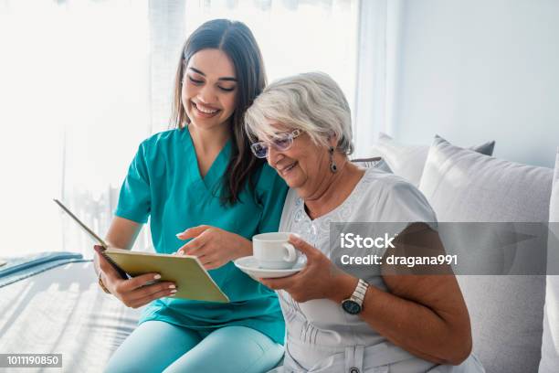 Donna Che Legge Un Libro Mentre È Seduta Con La Nonna Felice Che Beve Il Tè - Fotografie stock e altre immagini di Infermiera - Infermiere