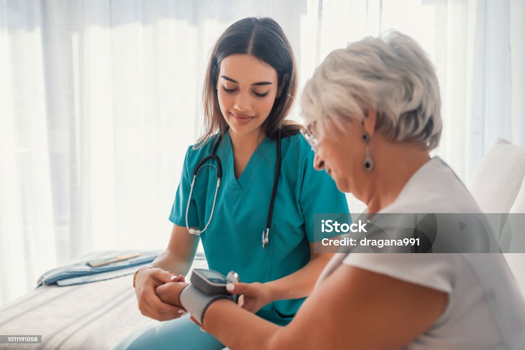 Young nurse measuring blood pressure of elderly woman at home Young nurse measuring blood pressure of elderly woman at home. Female nurse checking blood pressure of a senior woman at home,Home carer checking patients blood pressure Doctor Stock Photo