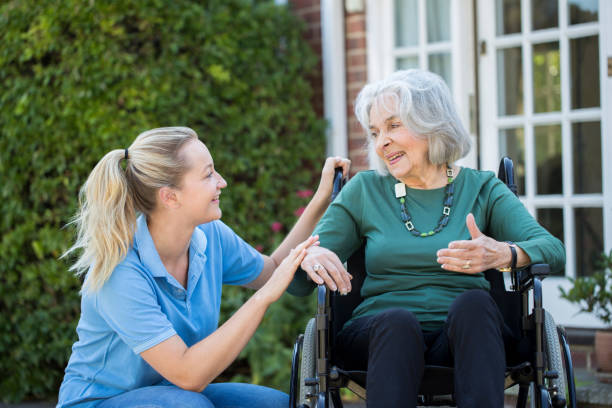 empujando la mujer senior en silla de ruedas exterior casa del cuidador - home health nurse fotografías e imágenes de stock