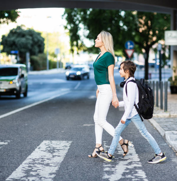 istock Elementary schoolboy with backpack and Mom crossing the road 1011231392