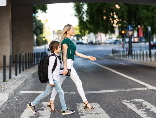 istock Elementary schoolboy with backpack and Mom crossing the road 1011231404