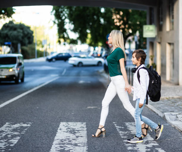 istock Elementary schoolboy with backpack and Mom crossing the road 1011231410