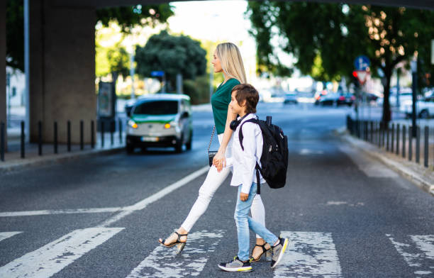 istock Elementary schoolboy with backpack and Mom crossing the road 1011231420