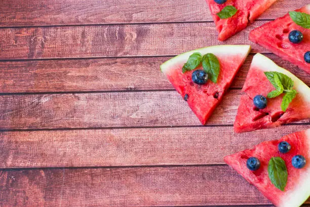 Photo of Pieces of sliced watermelon with mint and blueberries on a rustic dark background. Summer concept