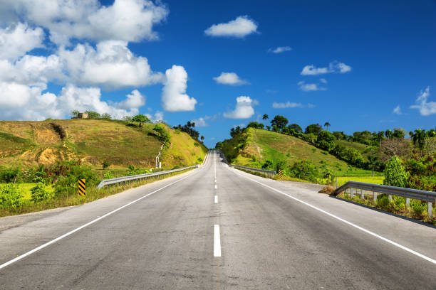 Empty asphalt road through the green field and clouds on blue sky background