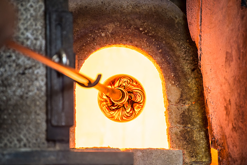 Murano glass-blowing factory. Glass blower forming beautiful piece of glass: put iron rod with attached glass object in furnace to make the glass malleable. Italy