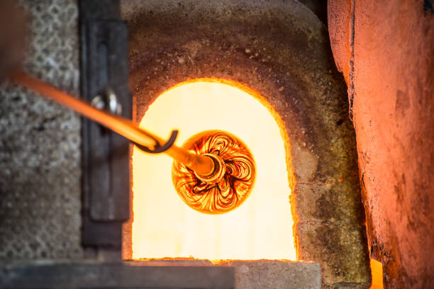 murano glass-blowing factory. glass blower forming beautiful piece of glass: put iron rod with attached glass object in furnace to make the glass malleable. italy - murano imagens e fotografias de stock