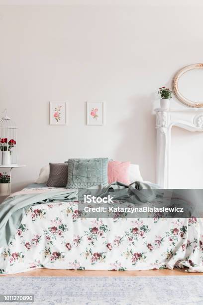 Two Simple Pink Posters Hanging On Wall Above Double Bed With Cushions And Floral Sheets In Real Photo Of White Bedroom Interior Stock Photo - Download Image Now