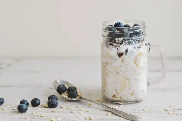 Overnight oats with whole grain cereal, fresh bluberries and coconut milk served with a spoon on wooden table. Healthy dessert for breakfast