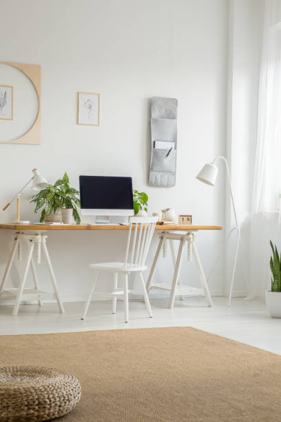 istock White chair at desk with computer desktop in home office interior with pouf on carpet. Real photo 1011288140