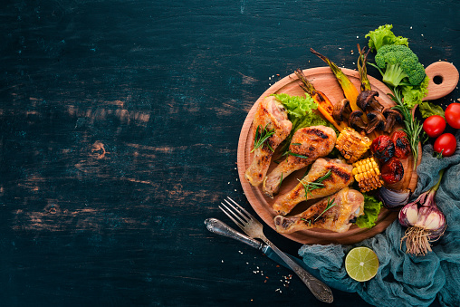 Baked chicken legs with spices and vegetables. On a wooden background. Top view. Copy space.