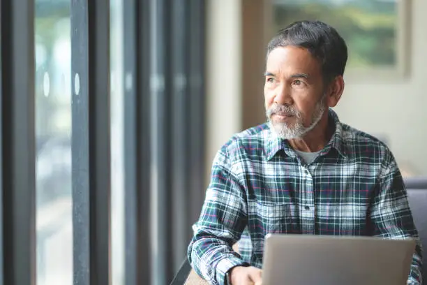 Photo of Mature man with white stylish short beard looking outside window. Casual lifestyle of retired hispanic people or adult asian man thinking and feeling confident sitting at modern coffee shop cafe.