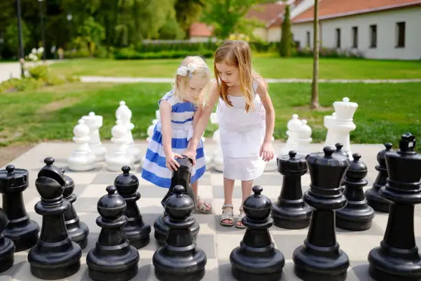 Two little sisters playing giant chess outdoors