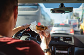 Man driving car while eating hamburger.