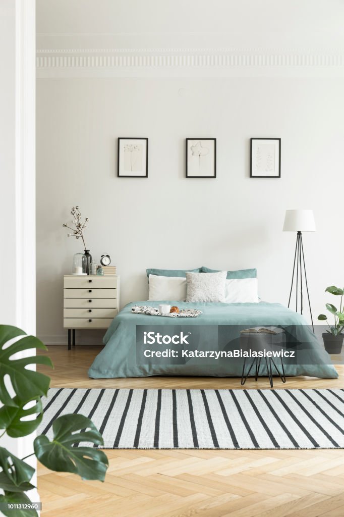 Real photo of bright bedroom interior with three simple posters, striped carpet and pastel green sheets on double bed Bedroom Stock Photo