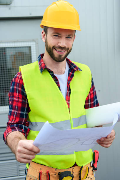 istock smiling engineer in safety vest and helmet working with blueprints 1011317452