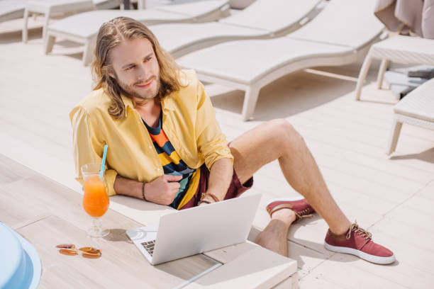 istock high angle view of smiling young man using laptop while resting with cocktail at poolside 1011331780