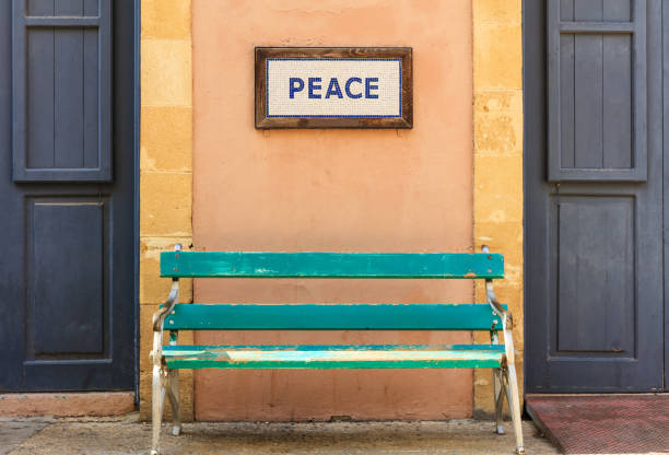 Word peace framed above an old wooden bench on a column between two doors. Close up view.