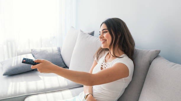 istock Relaxed young brunette woman lying on sofa and watching tv. 1011344458