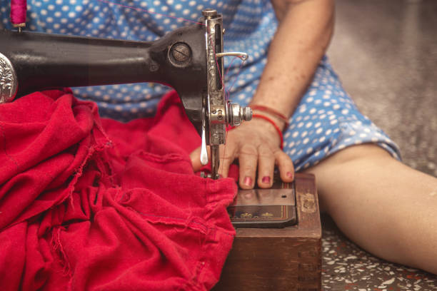 Indian Senior  women sitting cross-legged making clothes with old sewing machine