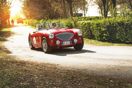 Ferrara / Italy - March 25, 2017: Classic vintage roadster: a red Austin Healey traveling in a country road at sunset