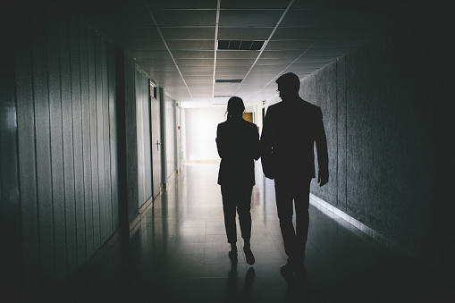 Handsome businessman and his colleague businesswoman walking in a dark hallway.