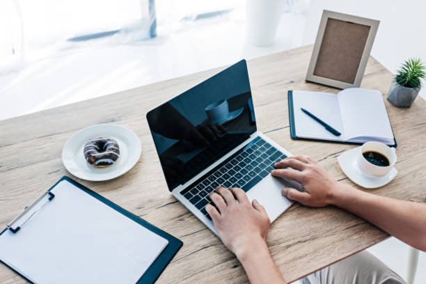 istock partial view of man with coffee cup and doughnut working at table with laptop, clipboard, textbook and photo frame 1011411250