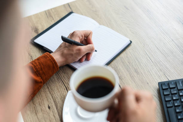 istock partial view of man writing in textbook and holding coffee cup at table with computer keyboard 1011411724