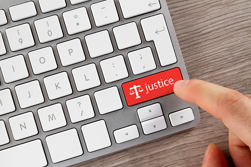 Index finger is pushing 'Justice' button on computer keyboard