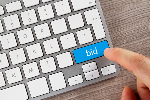 Index finger is pushing 'Bid' button on computer keyboard