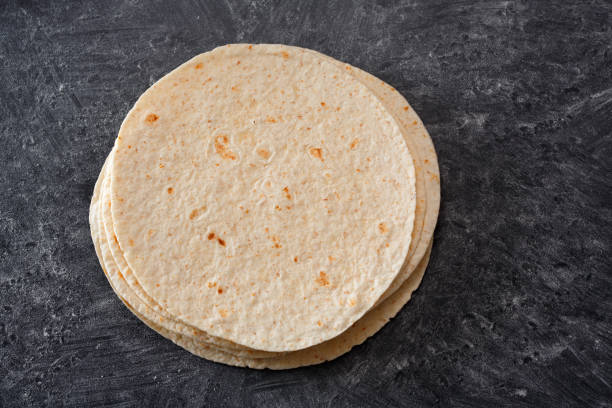 istock Stack of tortillas on a black table sprinkled with flour. Top view. 1011451924
