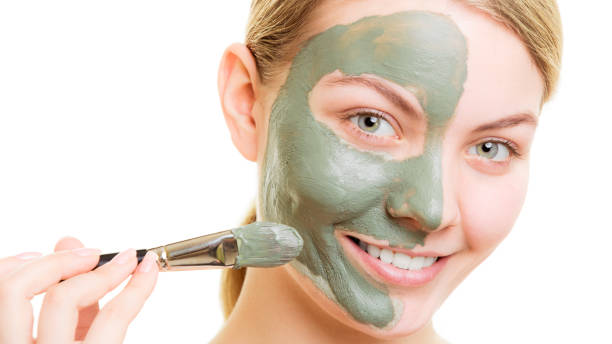 istock Woman applying with brush clay mud mask her face 1011454888