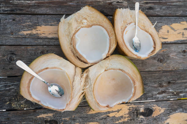 Two fresh halved coconuts with soft coconut meat on wooden background and two spoons.
