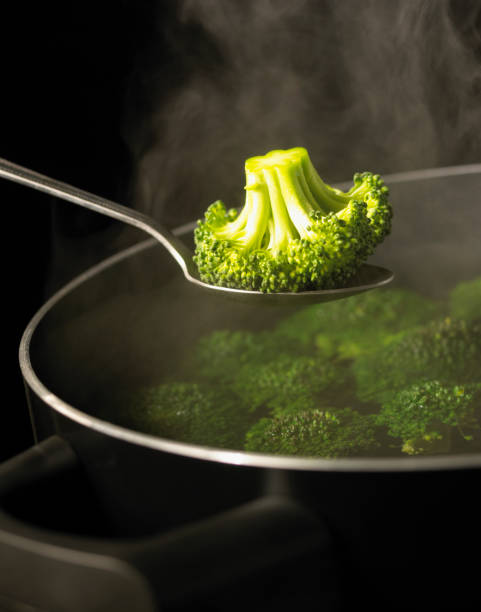 SPOON HOLDING BROCCOLI OVER PAN OF BOILING WATER
