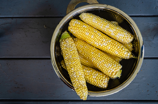 Top-down view of stainless steel bowl of sweet corn cobs on blue wooden table
