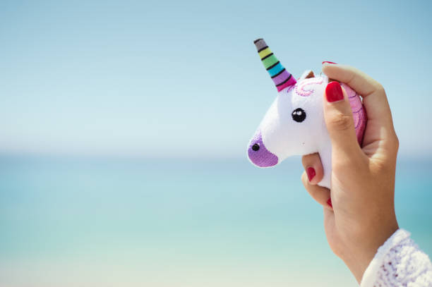 istock Hand holding pink trendy unicorn on blue sky background. Empty space. 1011539580