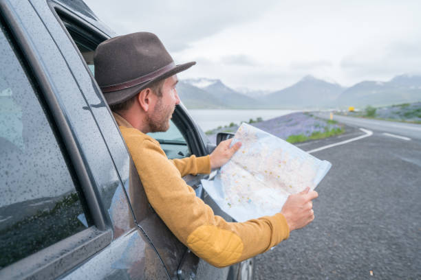 istock Young man in car looking at map, road trip concept vacations 1011555942