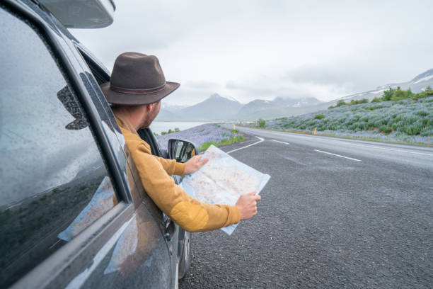 istock Young man in car looking at map, road trip concept vacations 1011556004
