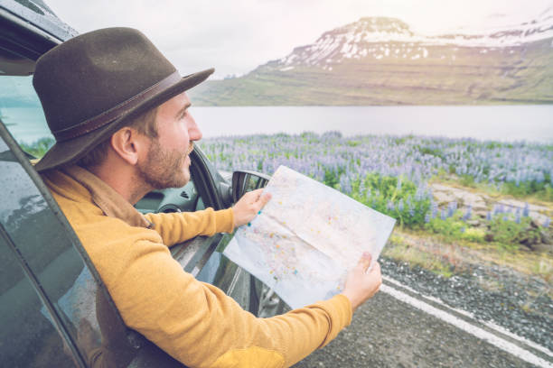 istock Young man in car looking at map, road trip concept vacations 1011556338